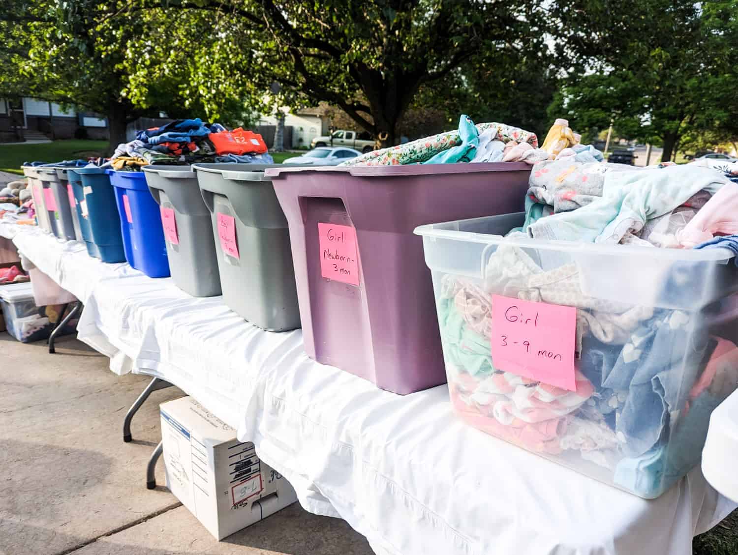 plastic tubs of organized childrens clothing displayed on tables at a garage sale