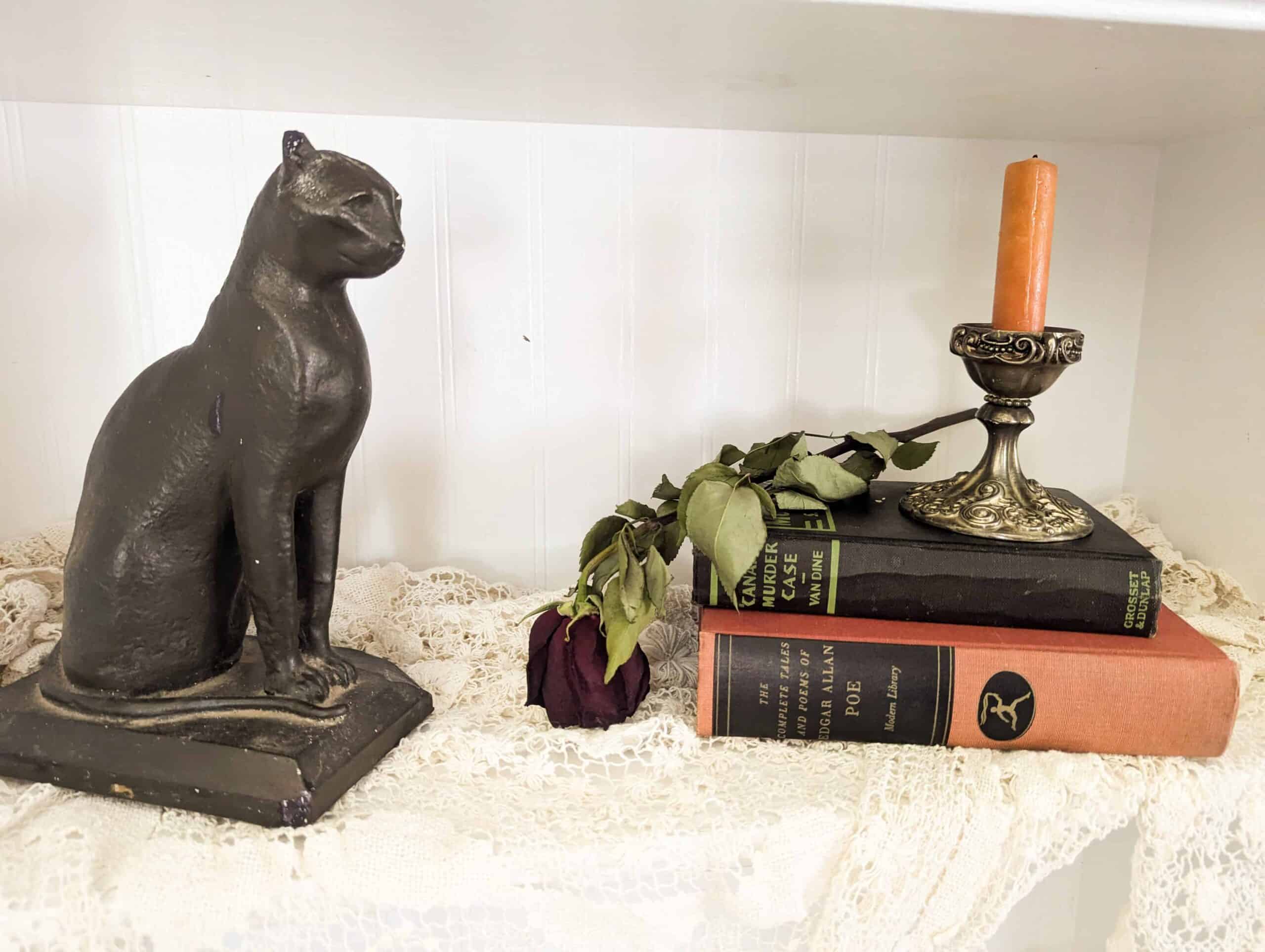 vintage black cat books dried rose and candlestick arranged as halloween decor on bookshelf